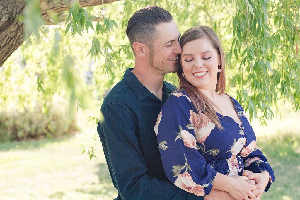 an engaged couple posing under a willow tree by Adrienne and Dani Photography
