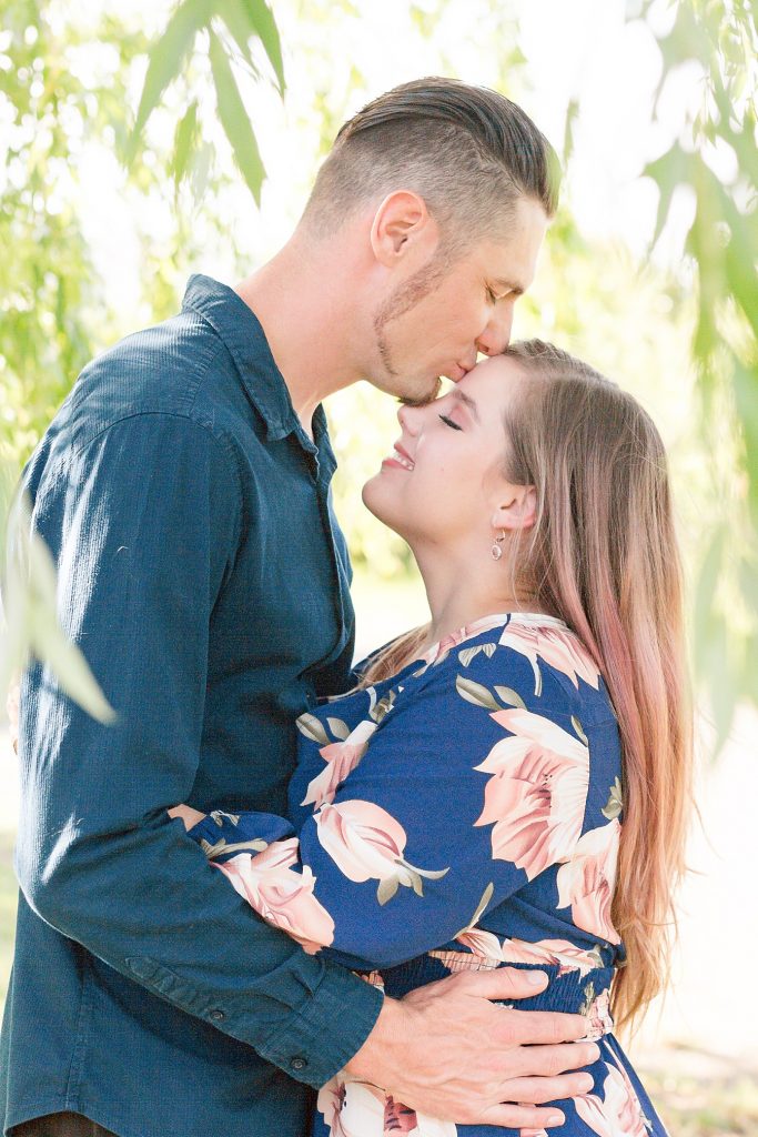 engaged couple posing under a willow tree by Adrienne and Dani Photography