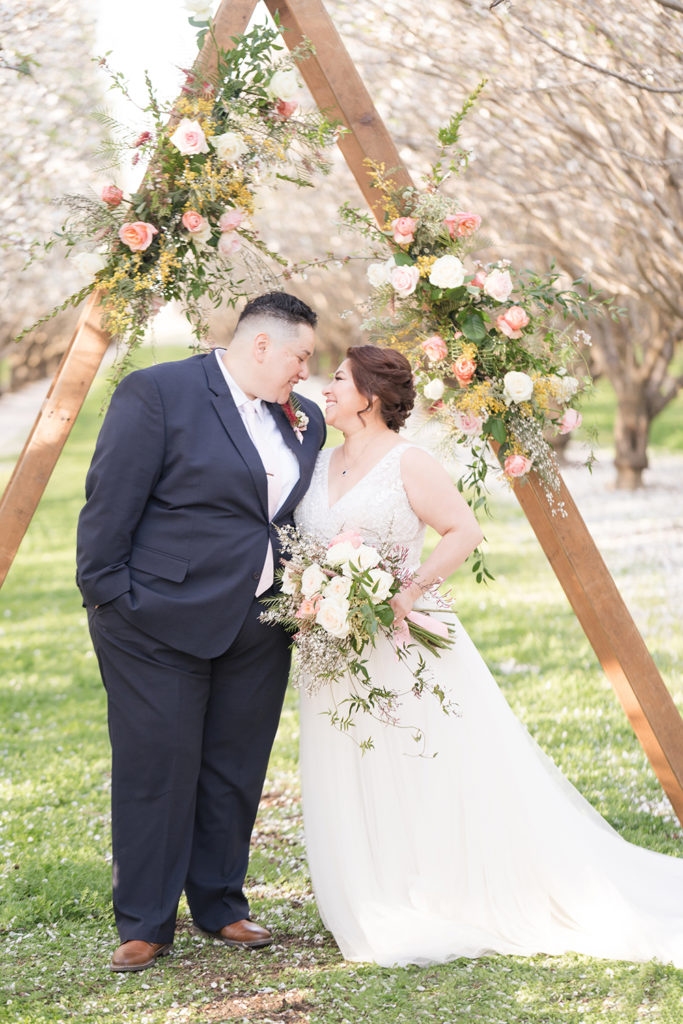 a couple poses under their wedding ceremony arch for their wedding portraits