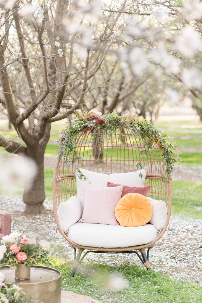 a wicker egg chair nestled in the almond blossoms for a wedding reception
