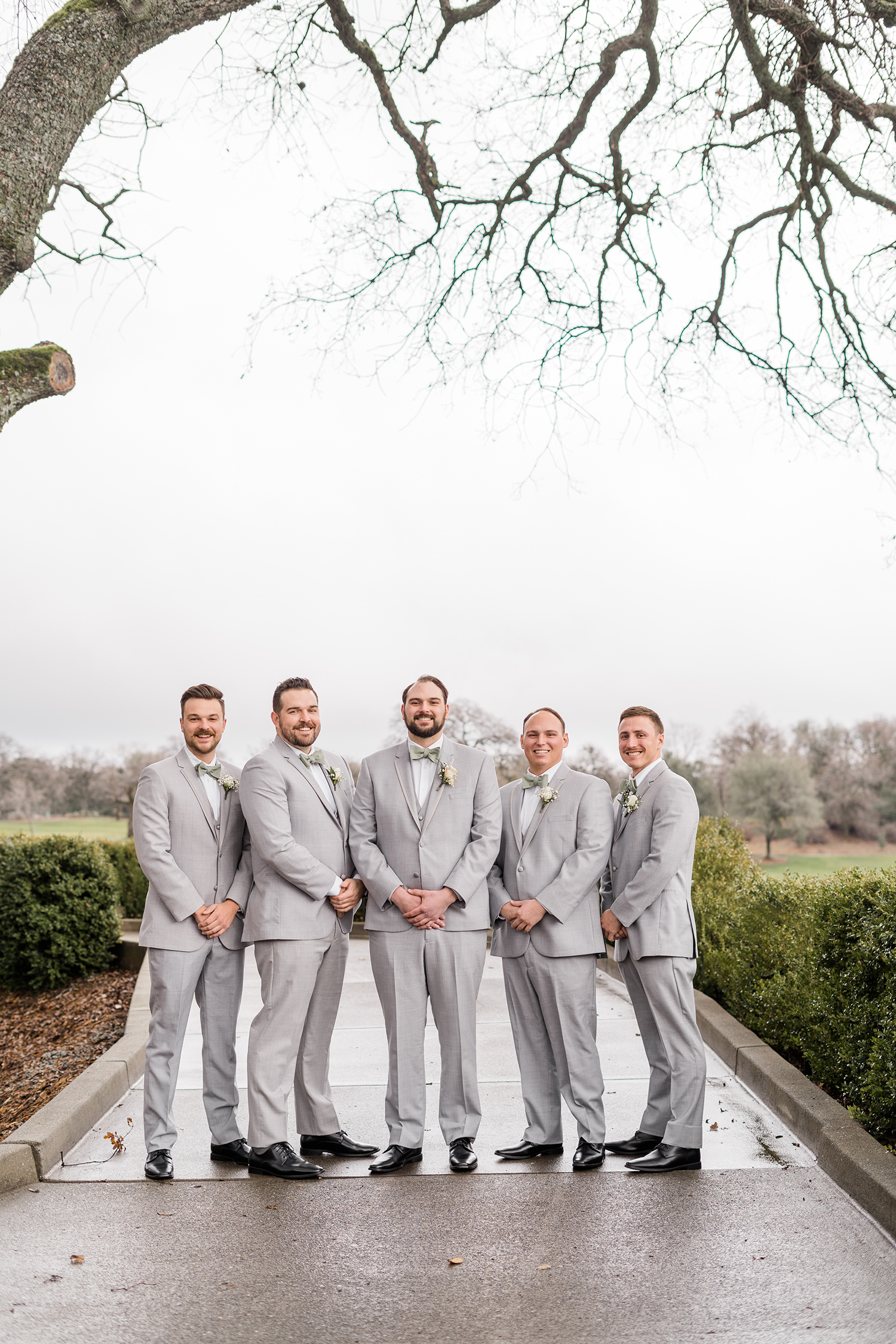 a wedding party in grey suits and sage green dresses at a wedding at the Ridge Event Center by Adrienne and Dani Photography