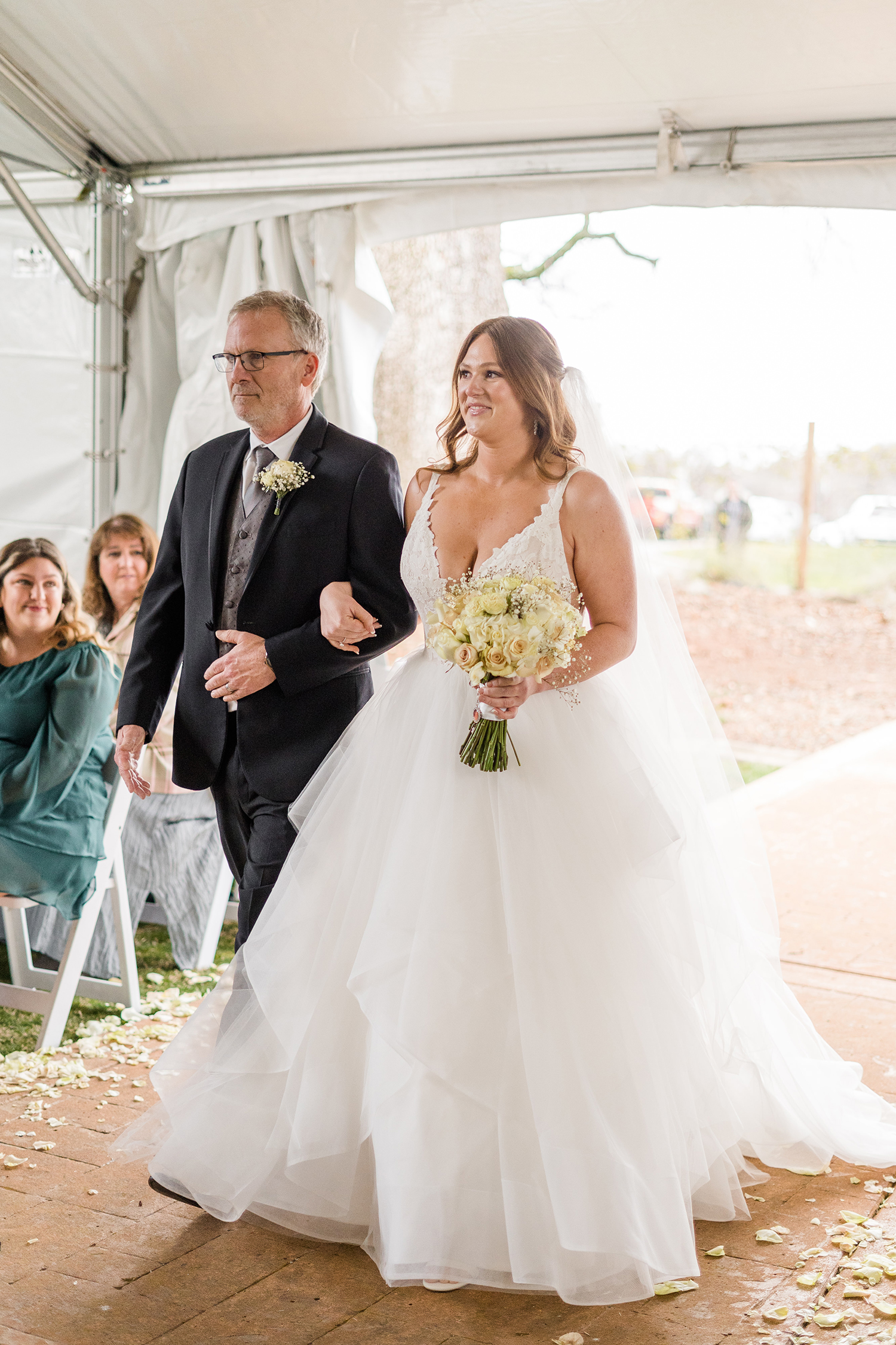 a brides smiles with her father as she walks down the aisle at her wedding at the Ridge Event Center by Adrienne and Dani Photography
