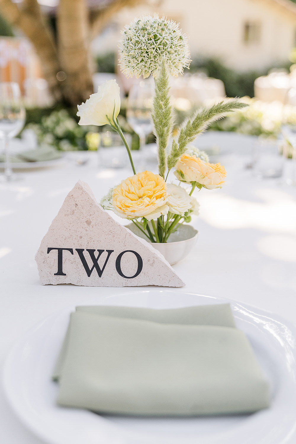 a reception table set up with white and sage green table linens and custom stone table numbers at a Piedmont Park Wedding