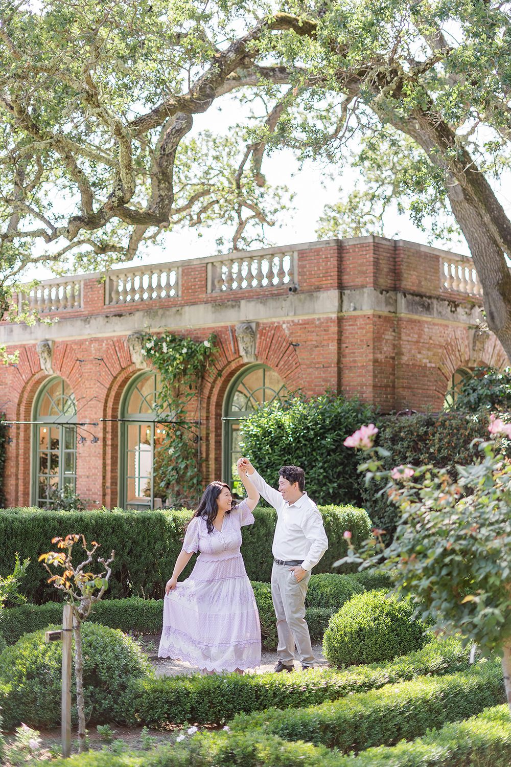 a bride and groom to-be dance together in front of a brick building for their filoli gardens engagement photos,