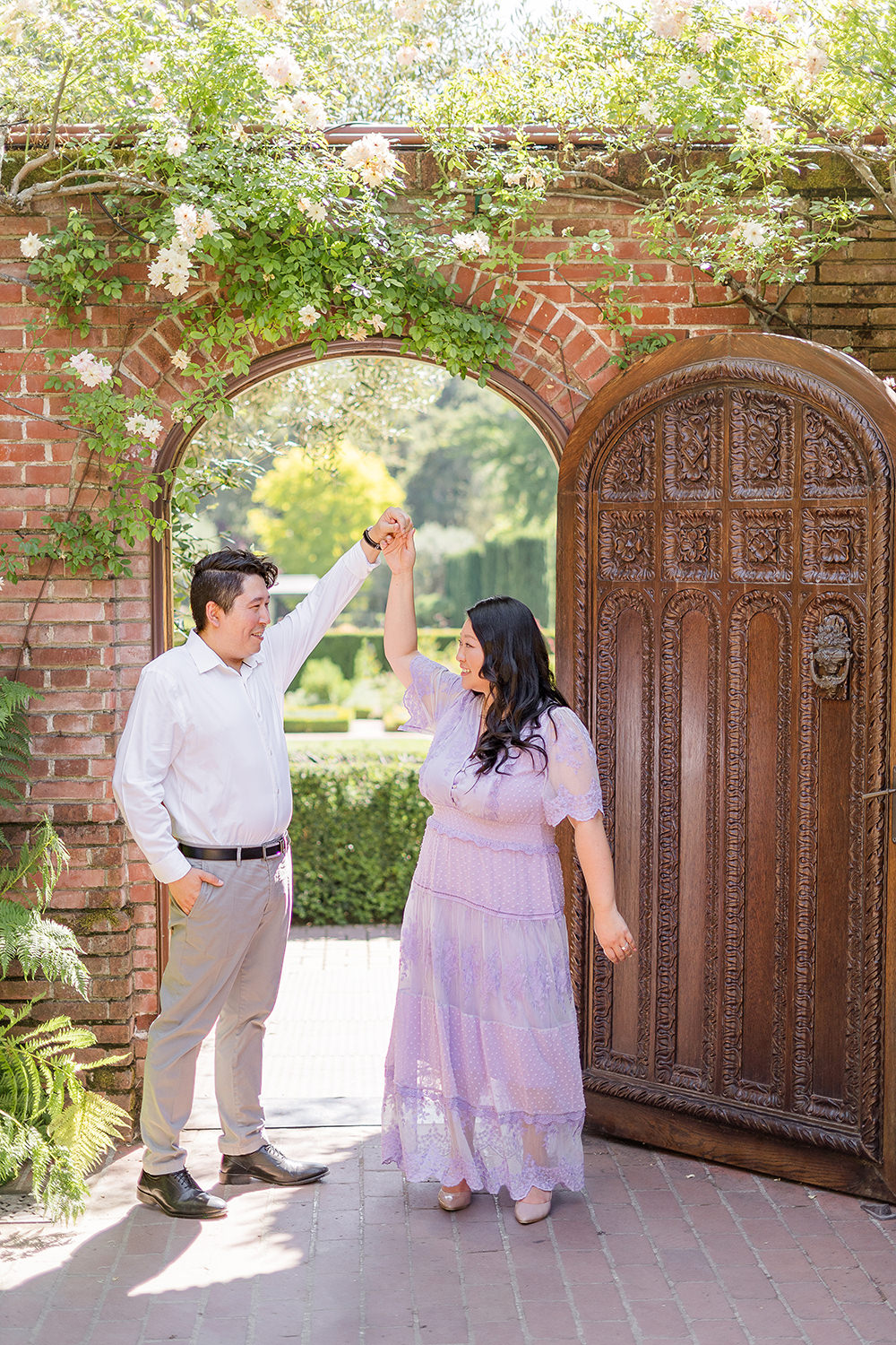 a bride and groom to-be dance together in front of a brick doorway for their filoli gardens engagement photos,