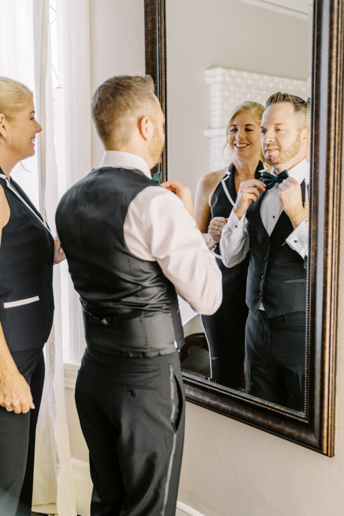 a groom adjusts his bow tie as he gets ready for his Downtown Sacramento Vizcaya Wedding