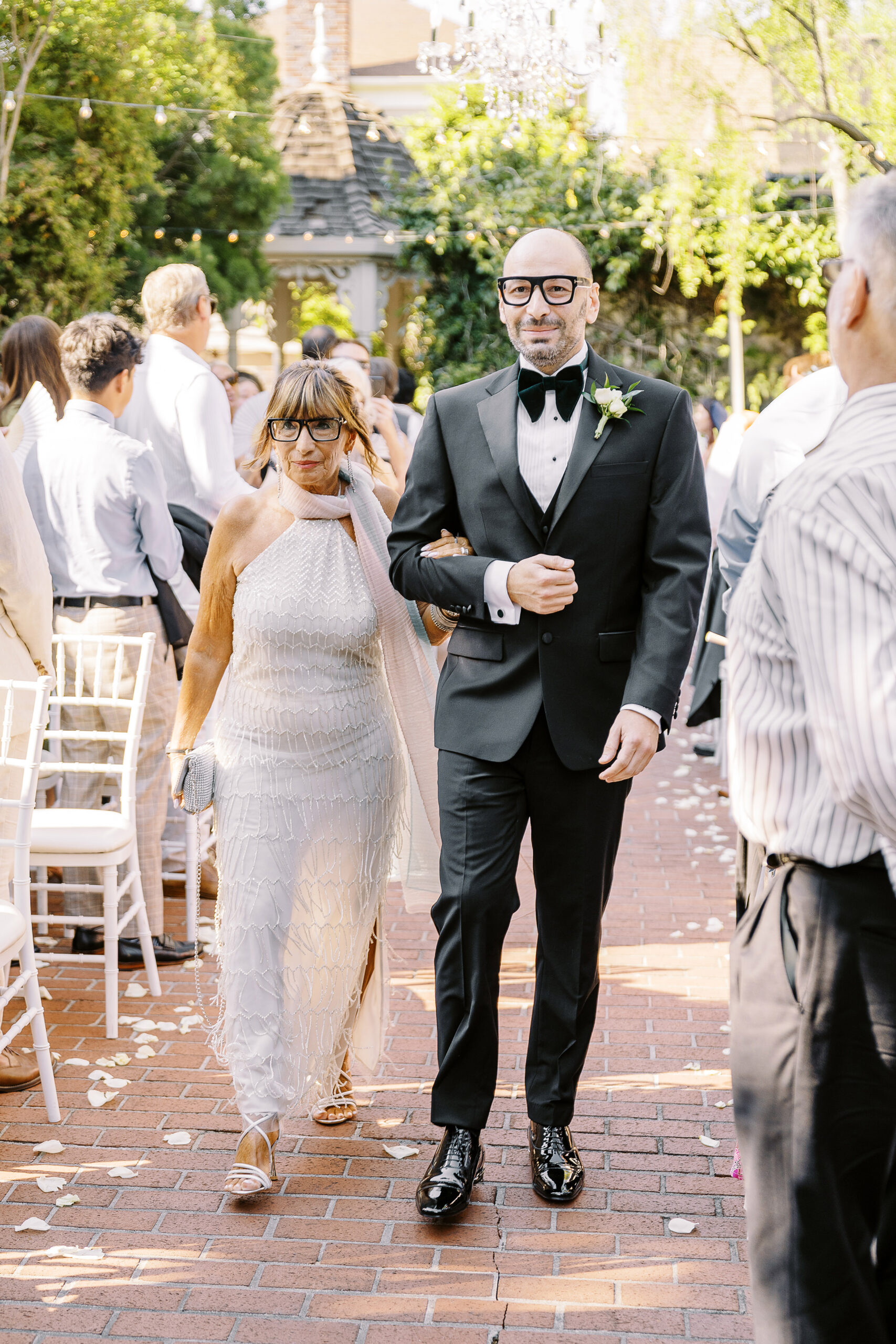 a groom walks down the aisle escorted by his mother at a Downtown Sacramento Vizcaya Wedding 