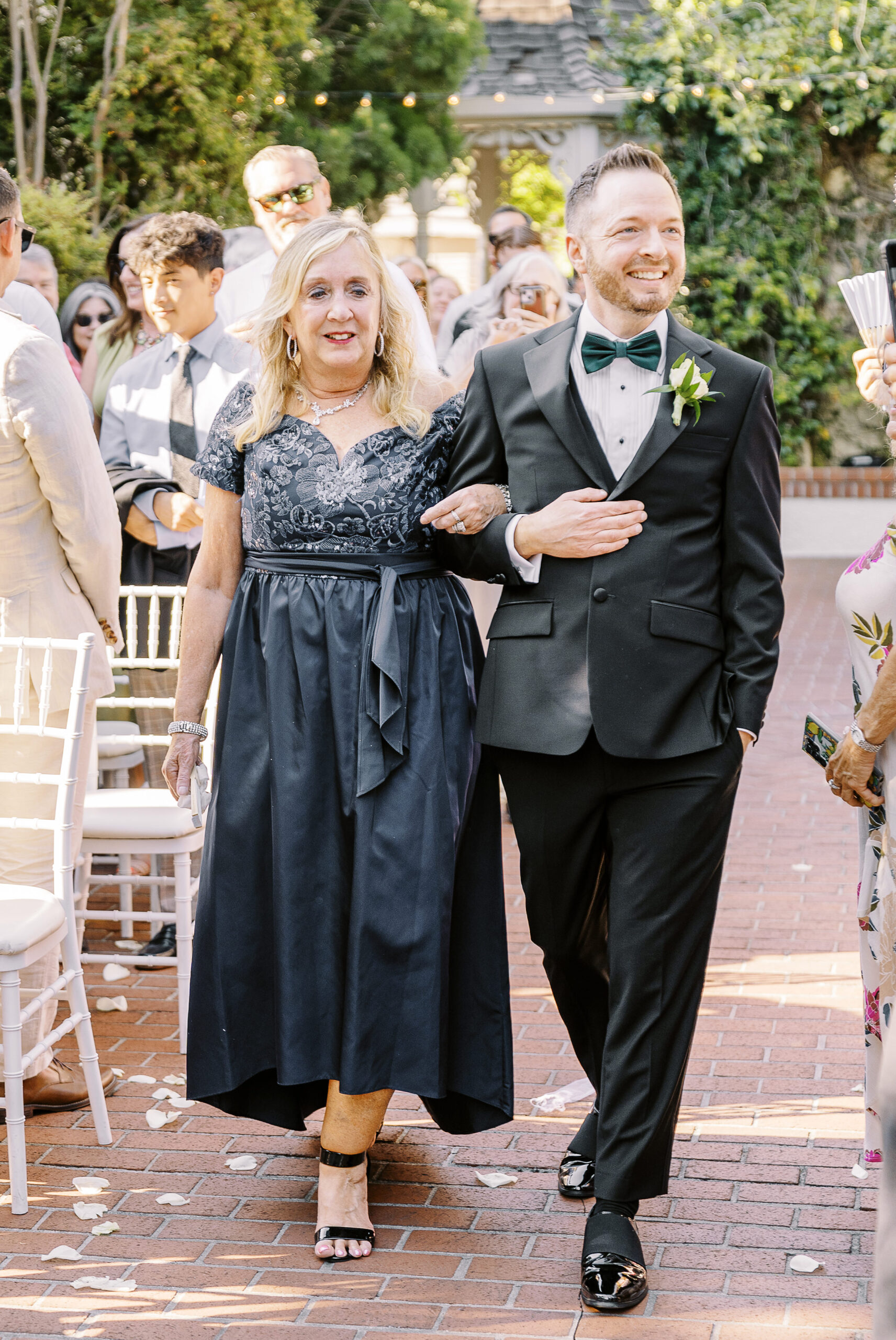 a groom walks down the aisle escorted by his mother at a Downtown Sacramento Vizcaya Wedding 