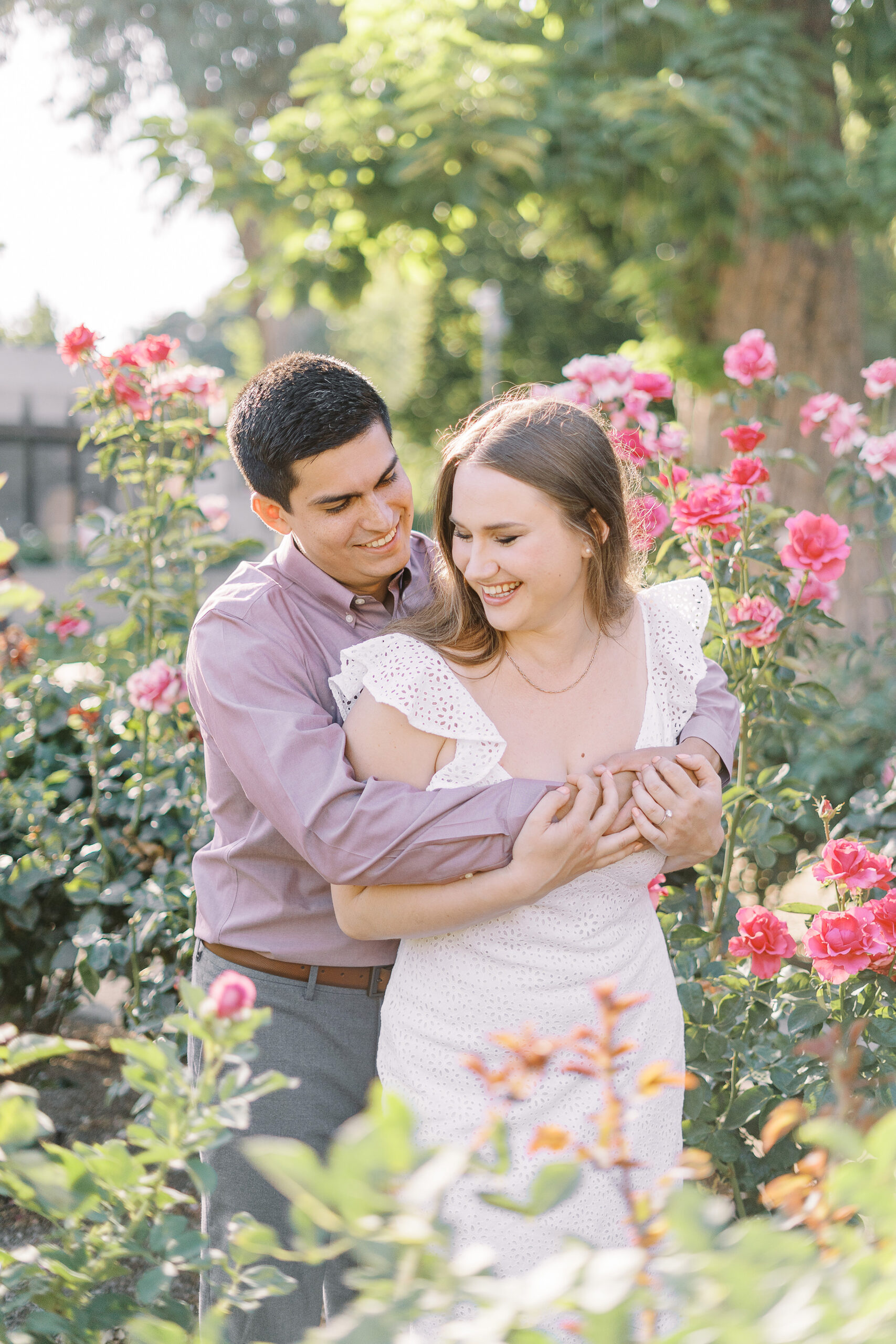 an engaged couple shares a hug in the roses of the Downtown Sacramento Capitol rose garden