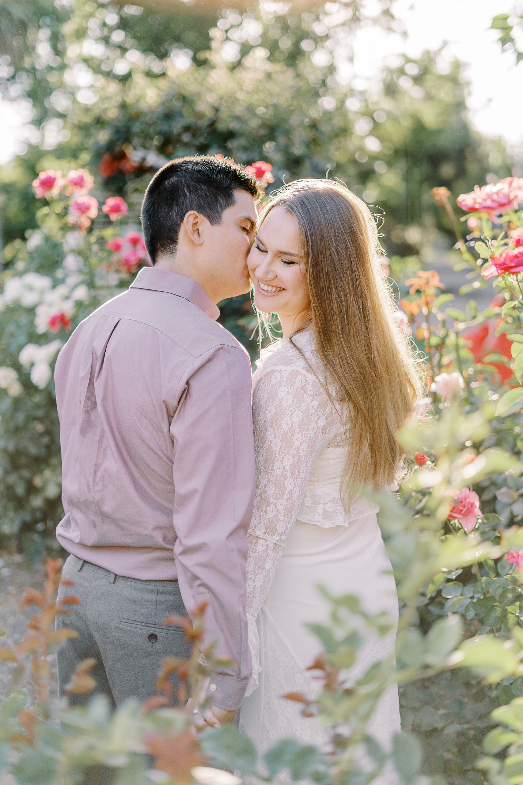 an engaged couple shares a kiss in the roses of the Downtown Sacramento Capitol rose garden