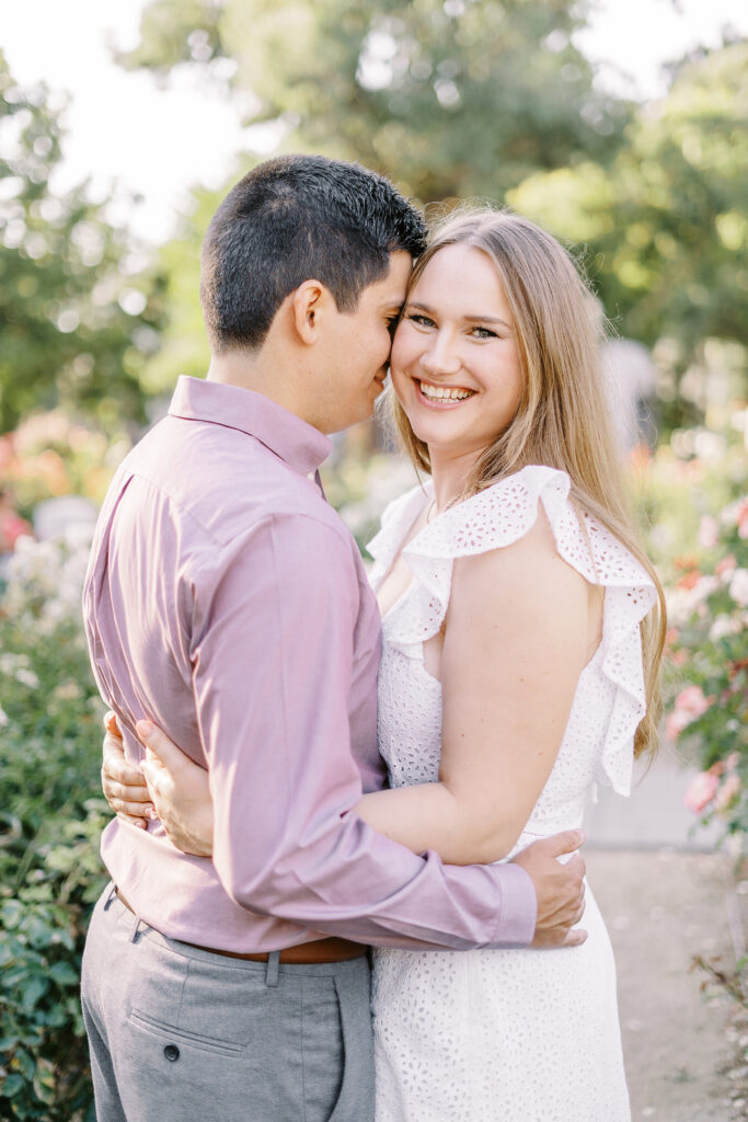 an engaged couple shares a hug in the roses of the Downtown Sacramento Capitol rose garden
