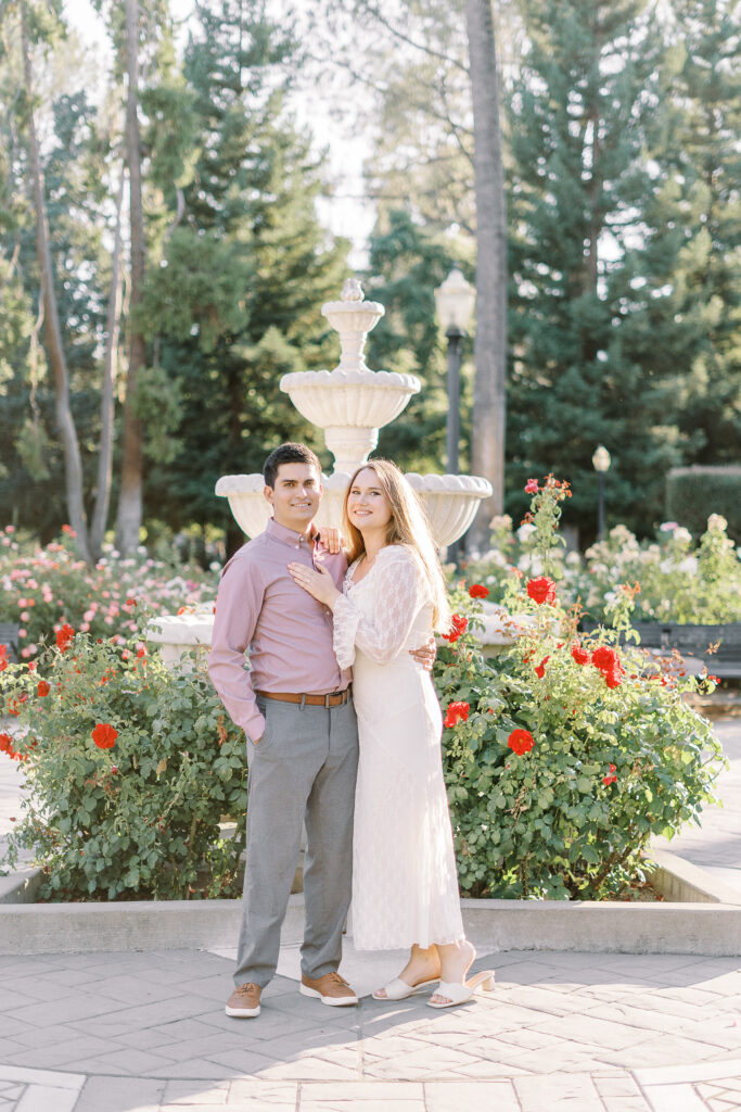 an engaged couple shares a hug in the roses of the Downtown Sacramento Capitol rose garden