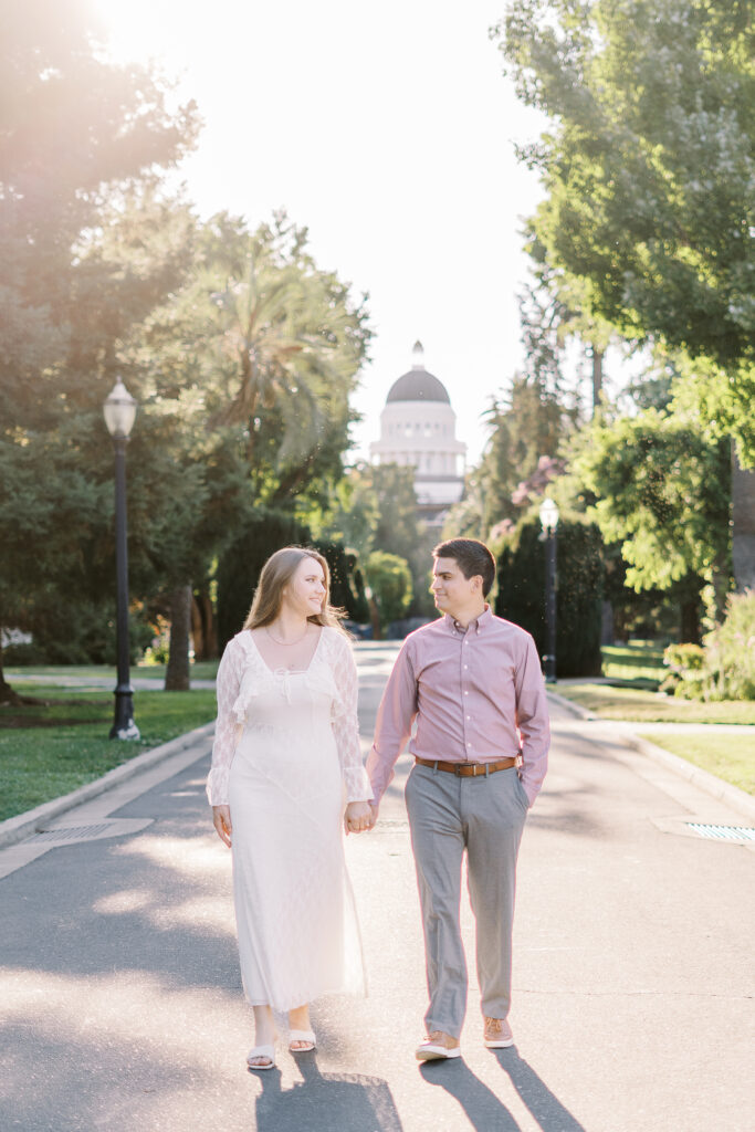 an engaged couple walks together holding hands in front of the Sacramento Capitol building for their Downtown Sacramento Capitol Engagement 