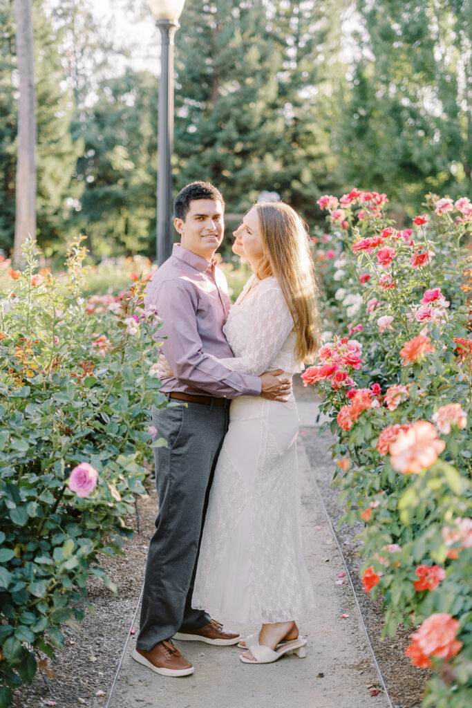 an engaged couple shares a hug in the roses of the Downtown Sacramento Capitol rose garden