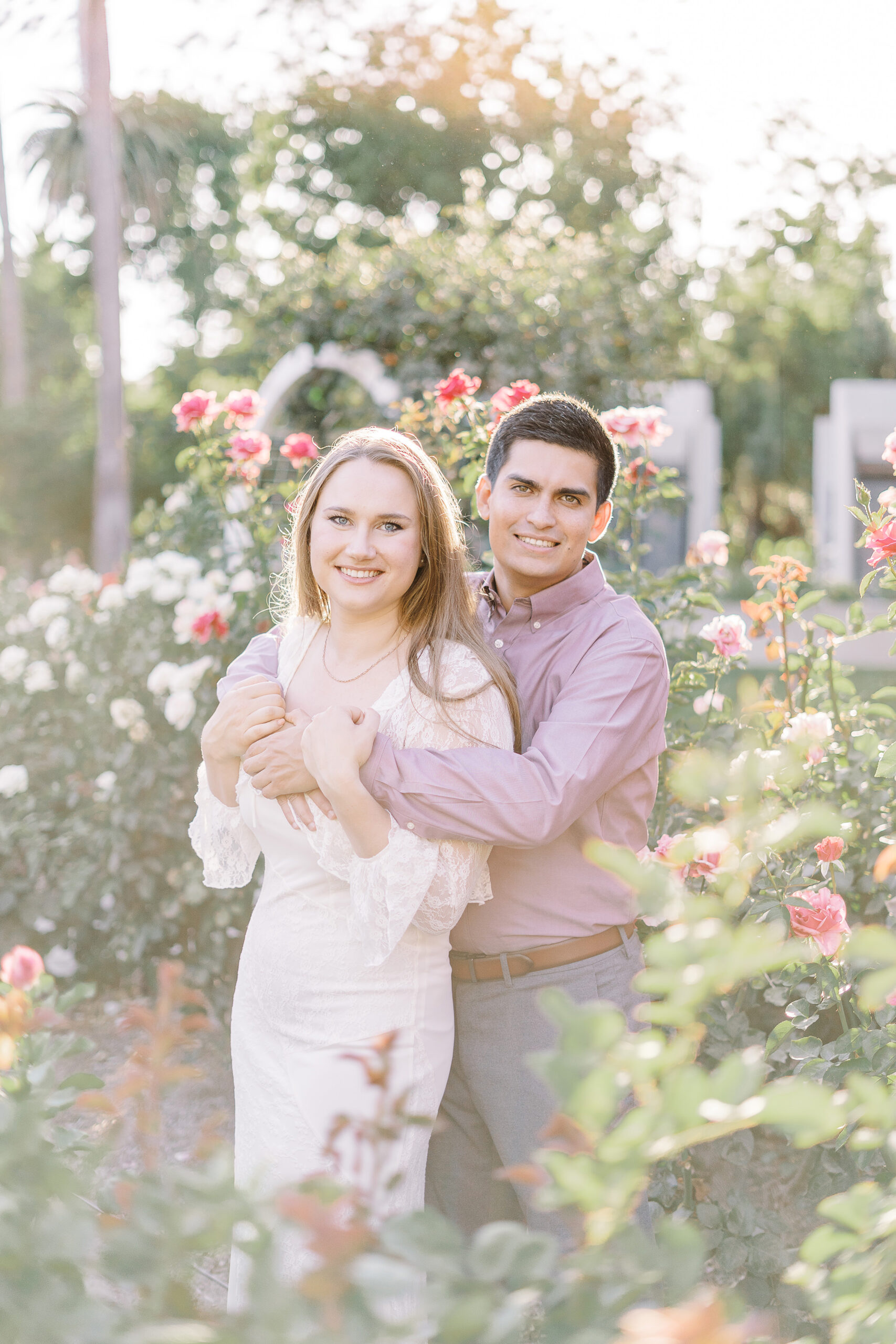 an engaged couple shares a hug in the roses of the Downtown Sacramento Capitol rose garden