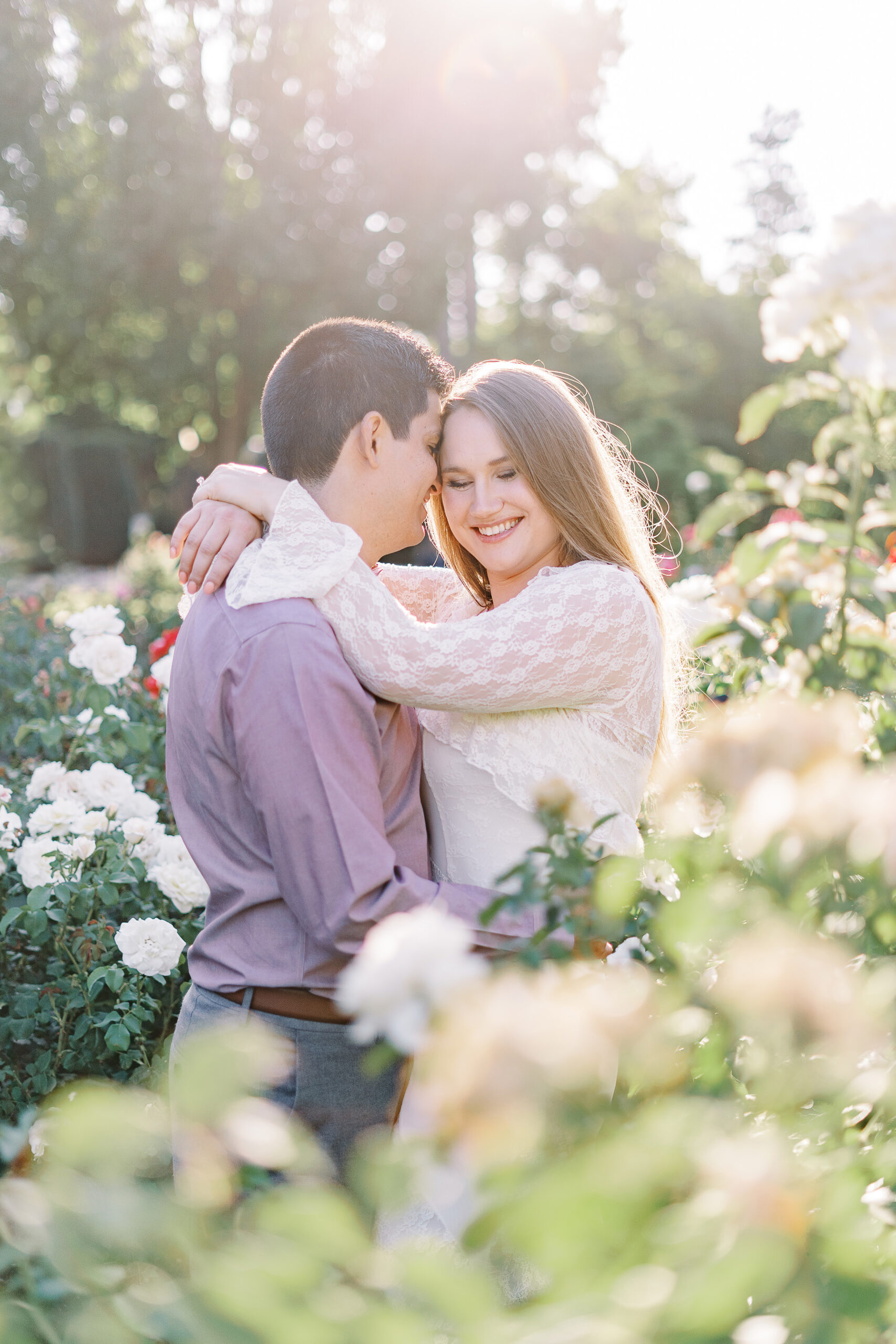 an engaged couple shares a hug in the roses of the Downtown Sacramento Capitol rose garden