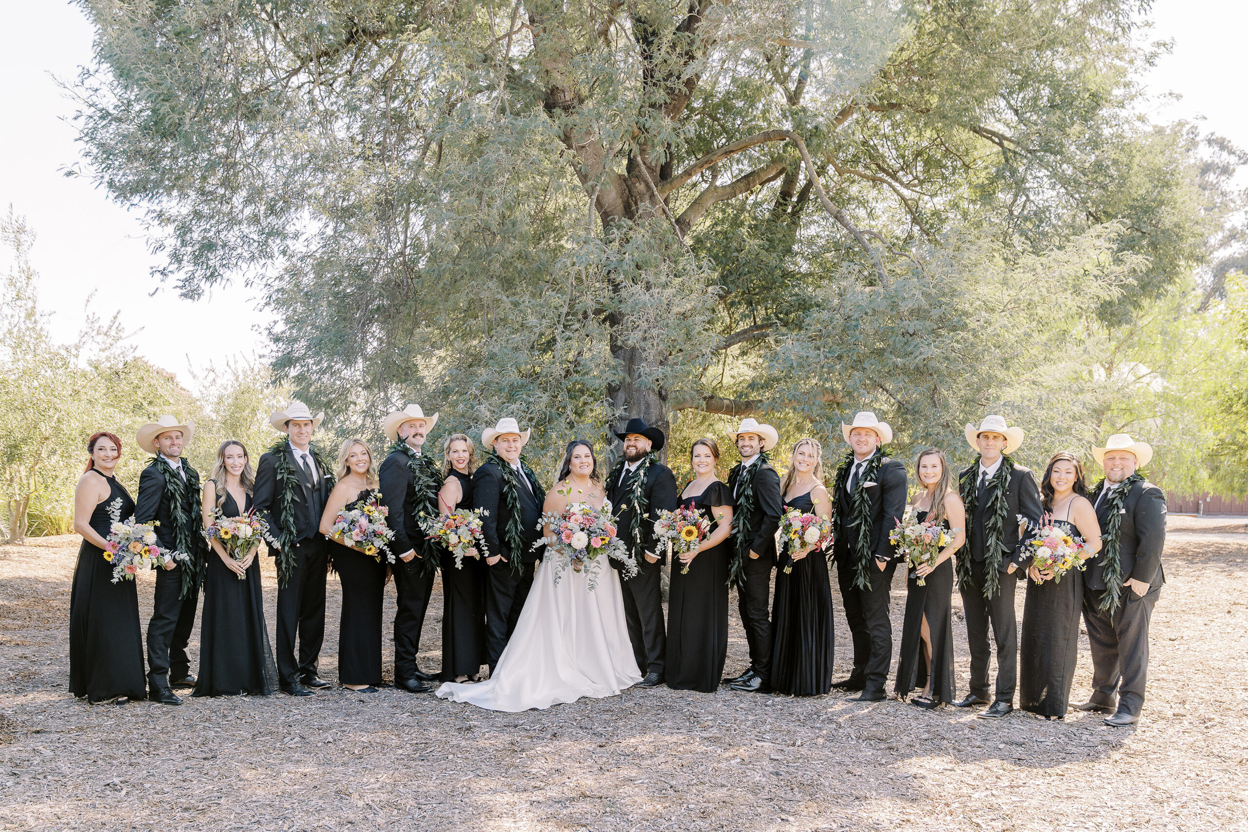 a large 18 person wedding party featuring black suits and white cowboy hats for the gentlemen and black dresses with colorful wildflower bouquets for the ladies for a sonoma winery wedding.