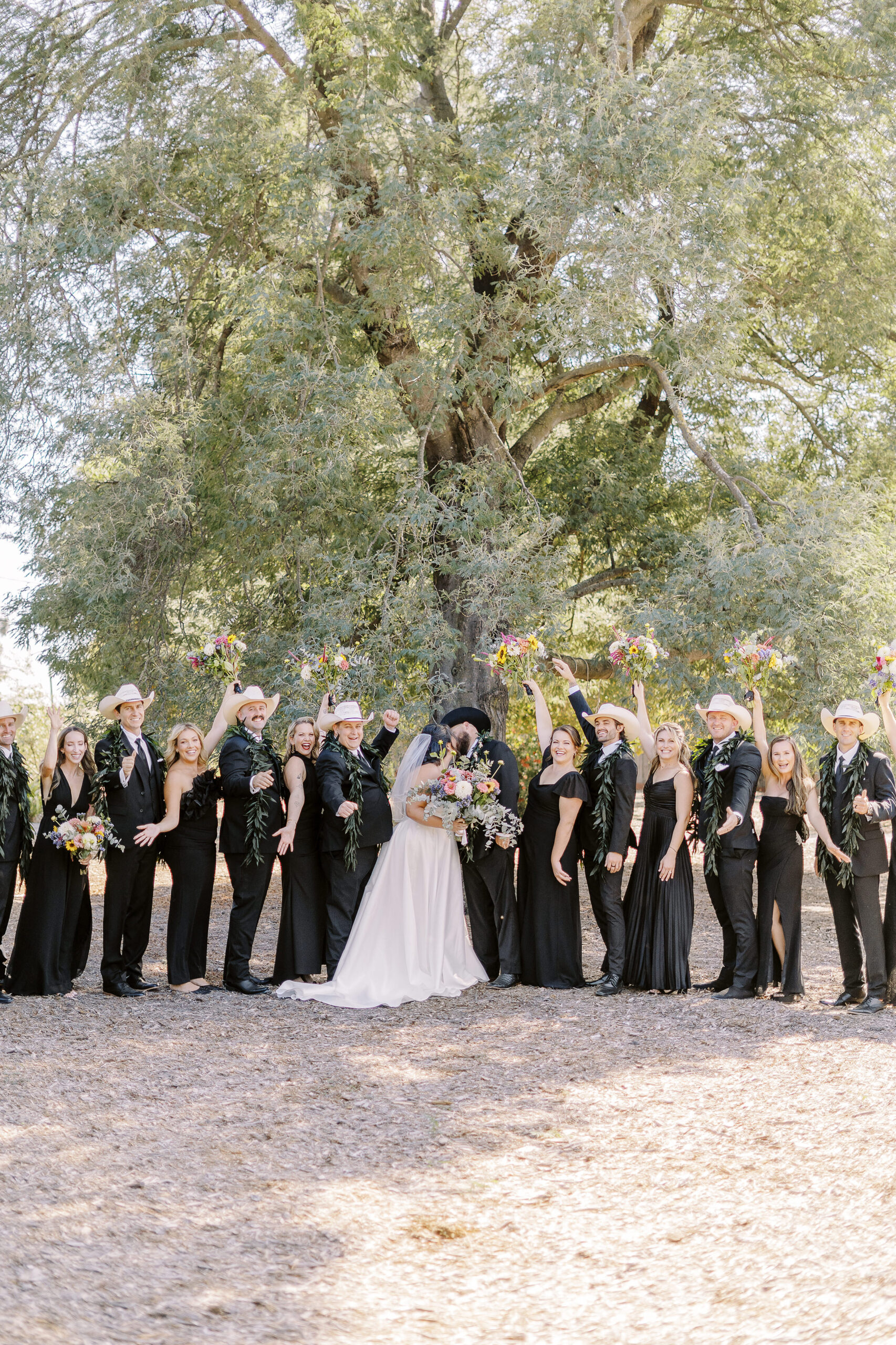 a large 18 person wedding party featuring black suits and white cowboy hats for the gentlemen and black dresses with colorful wildflower bouquets for the ladies for a sonoma winery wedding.