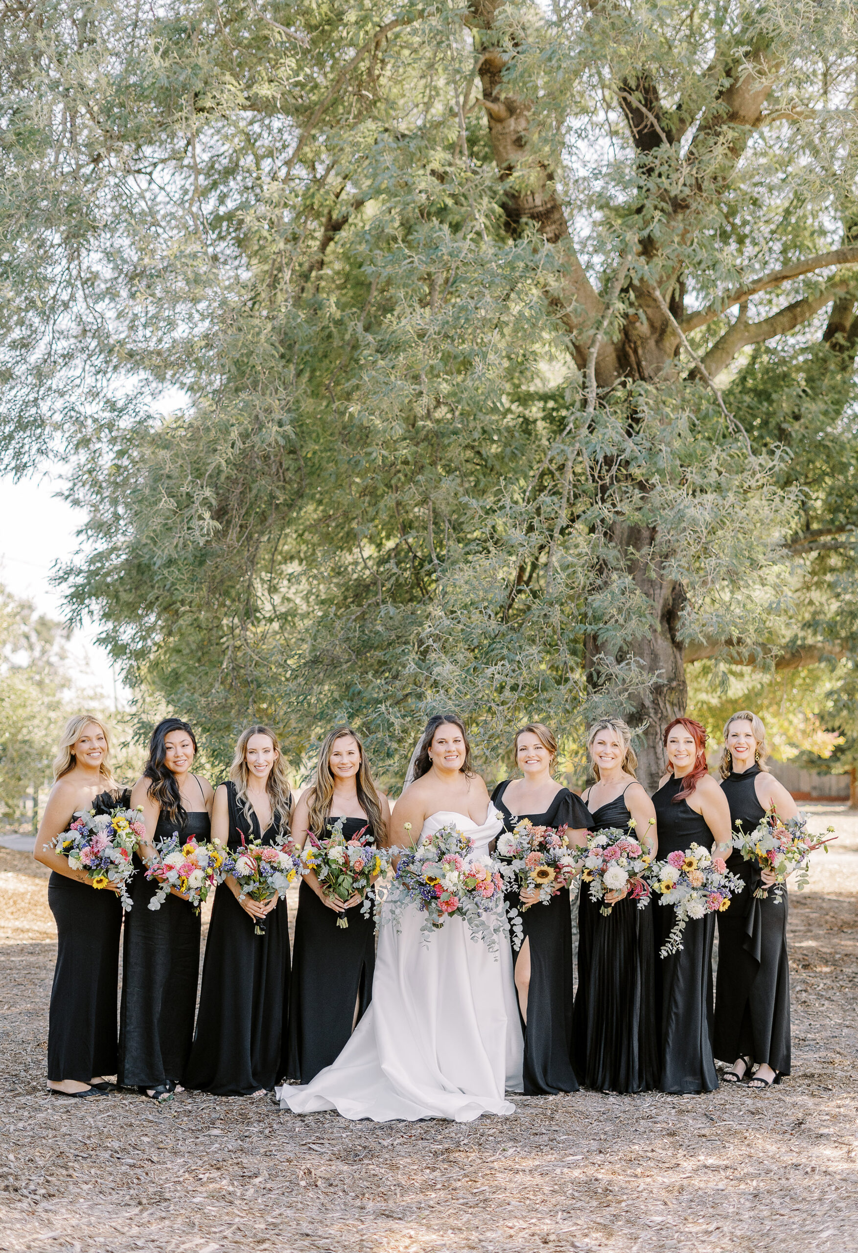 a large 18 person wedding party featuring black dresses with colorful wildflower bouquets for the ladies for a sonoma winery wedding.