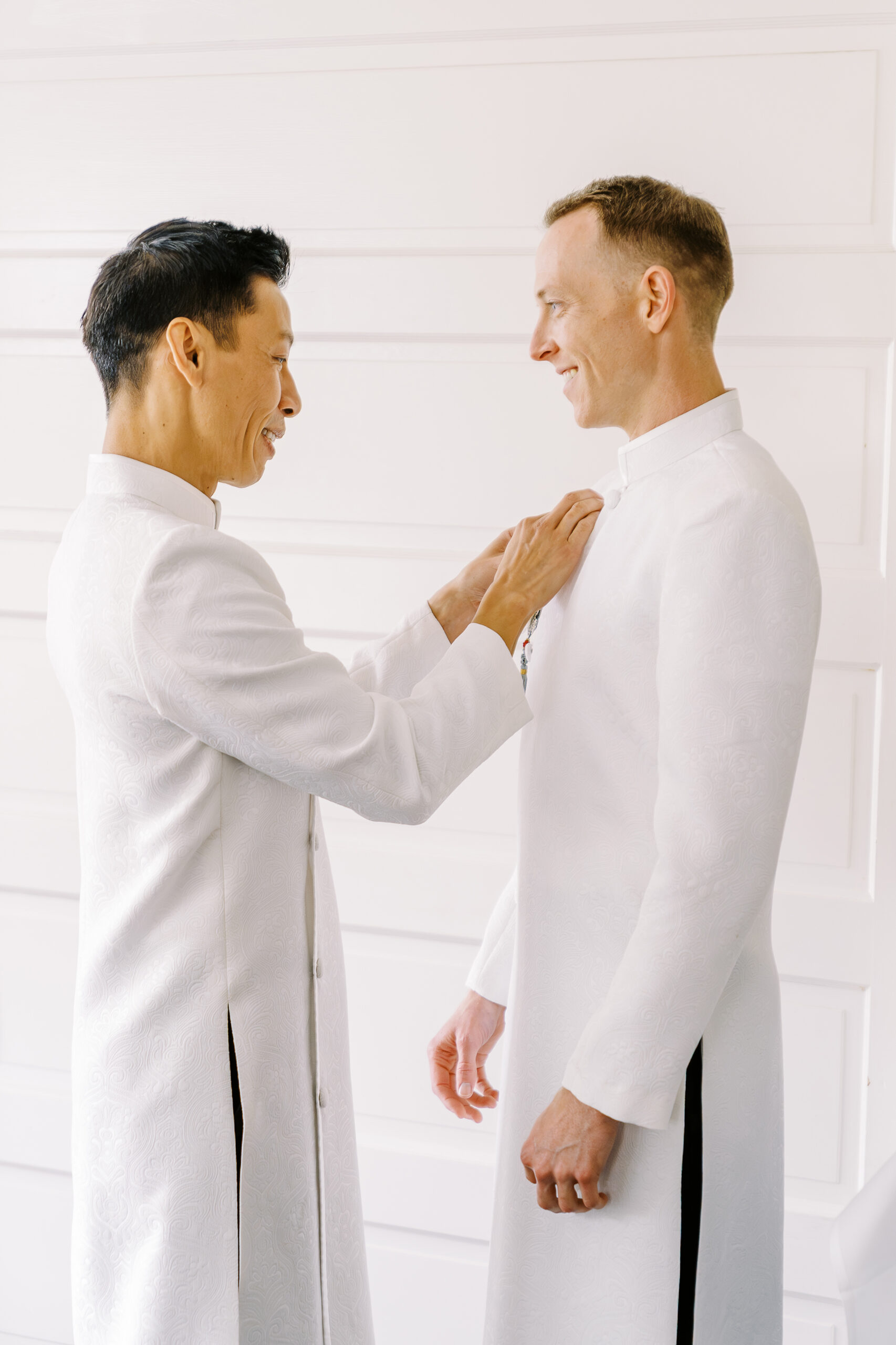a groom helps his fiance dress in a tradition ao dai for their wedding day.