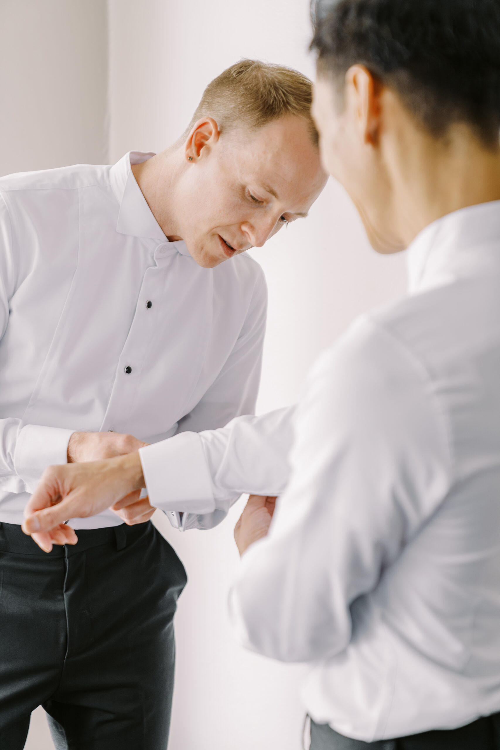 a groom helps his fiance button his shirt sleeve buttons while getting ready for their vizcaya sacramento wedding