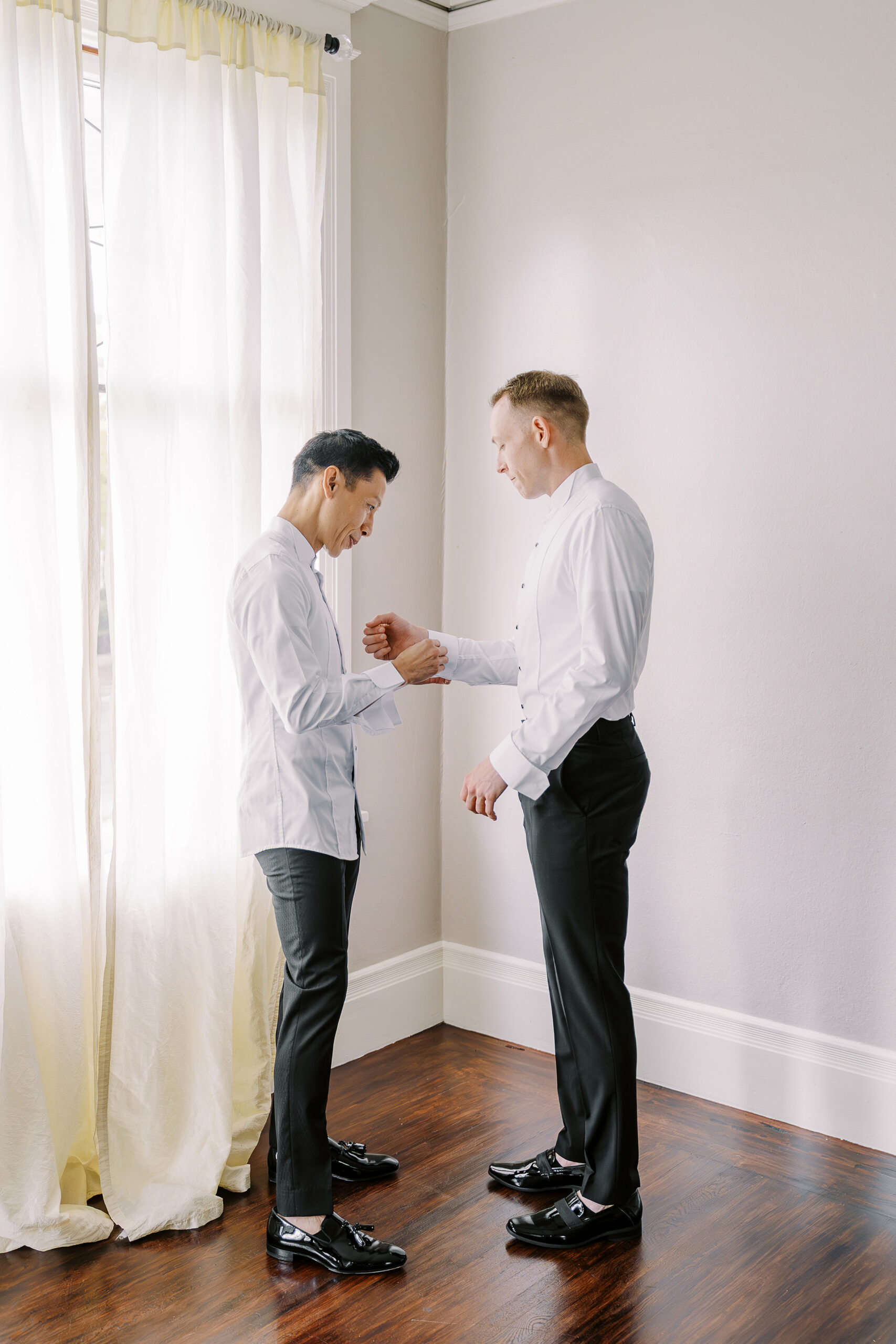 a groom helps his fiance button his shirt sleeve buttons while getting ready for their vizcaya sacramento wedding
