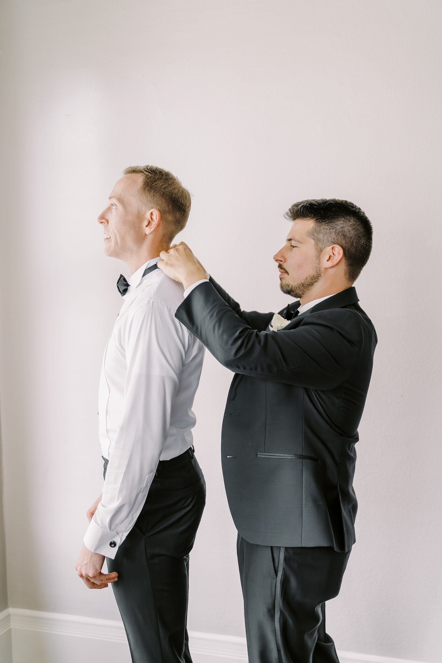a grooms friend helps him clasp his bowtie while getting ready for his vizcaya sacramento wedding