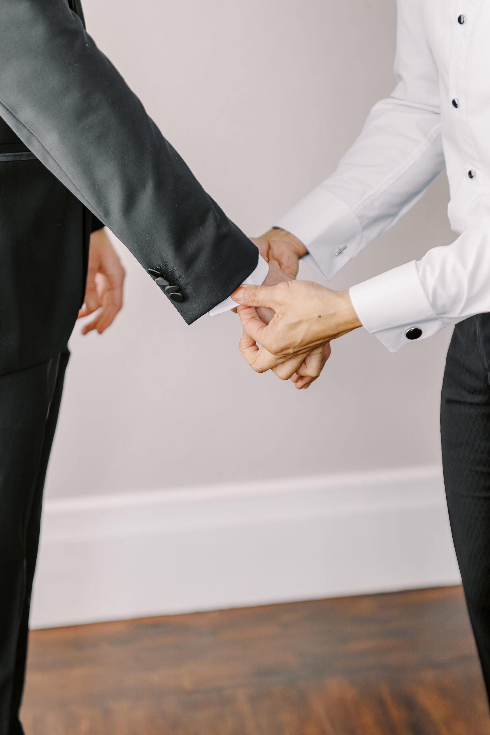 a groom helps his friend straighten his shirt sleeve cuff