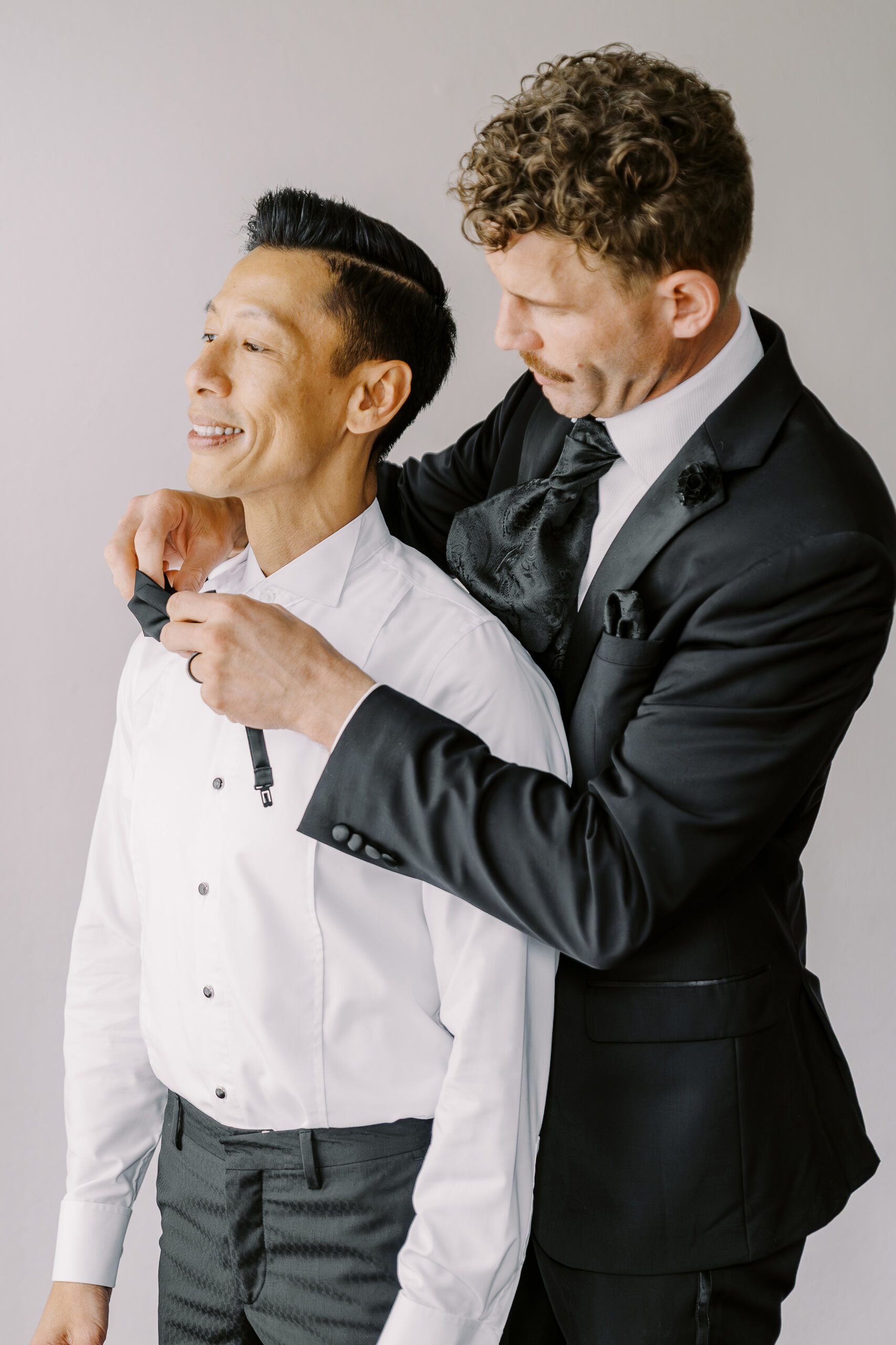 a grooms friend helps him clasp his bowtie while getting ready for his vizcaya sacramento wedding