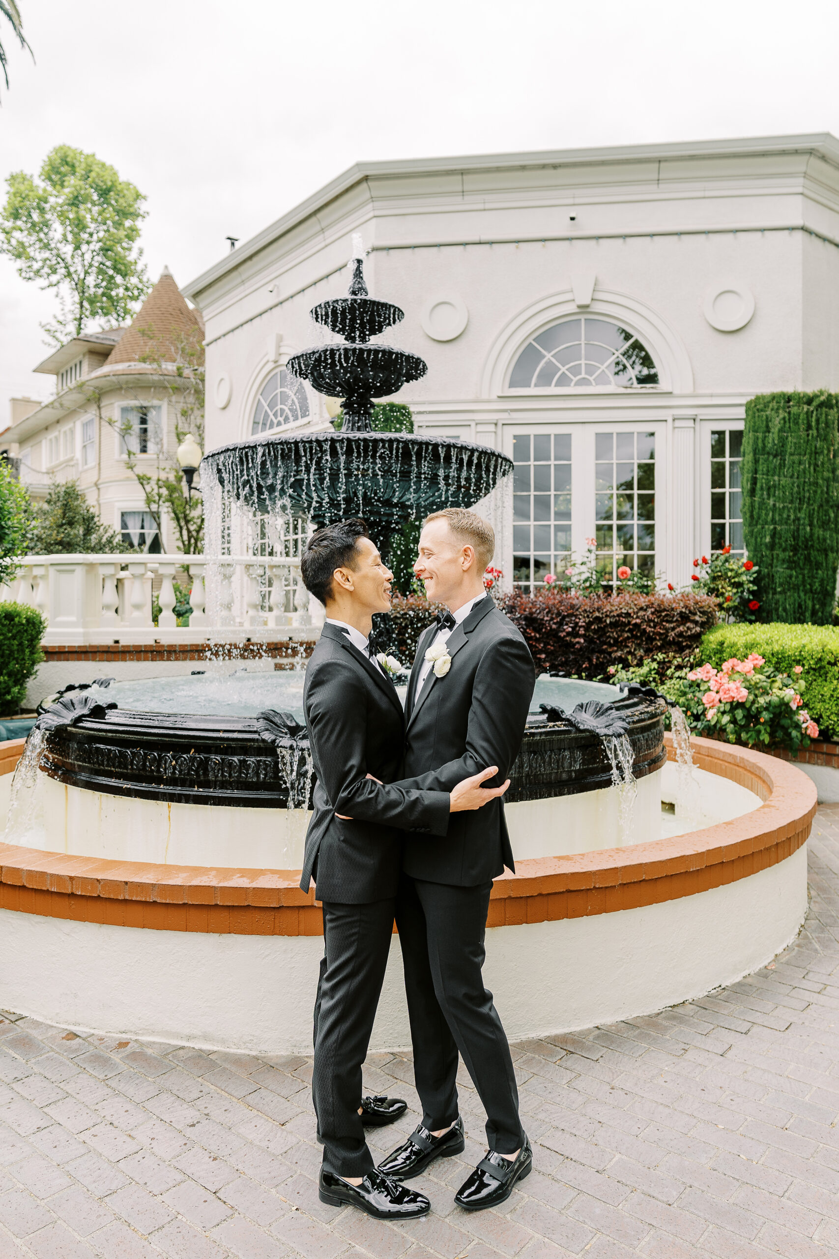 two groom embrace each other in front of the water fountain at their vizcaya sacramento wedding