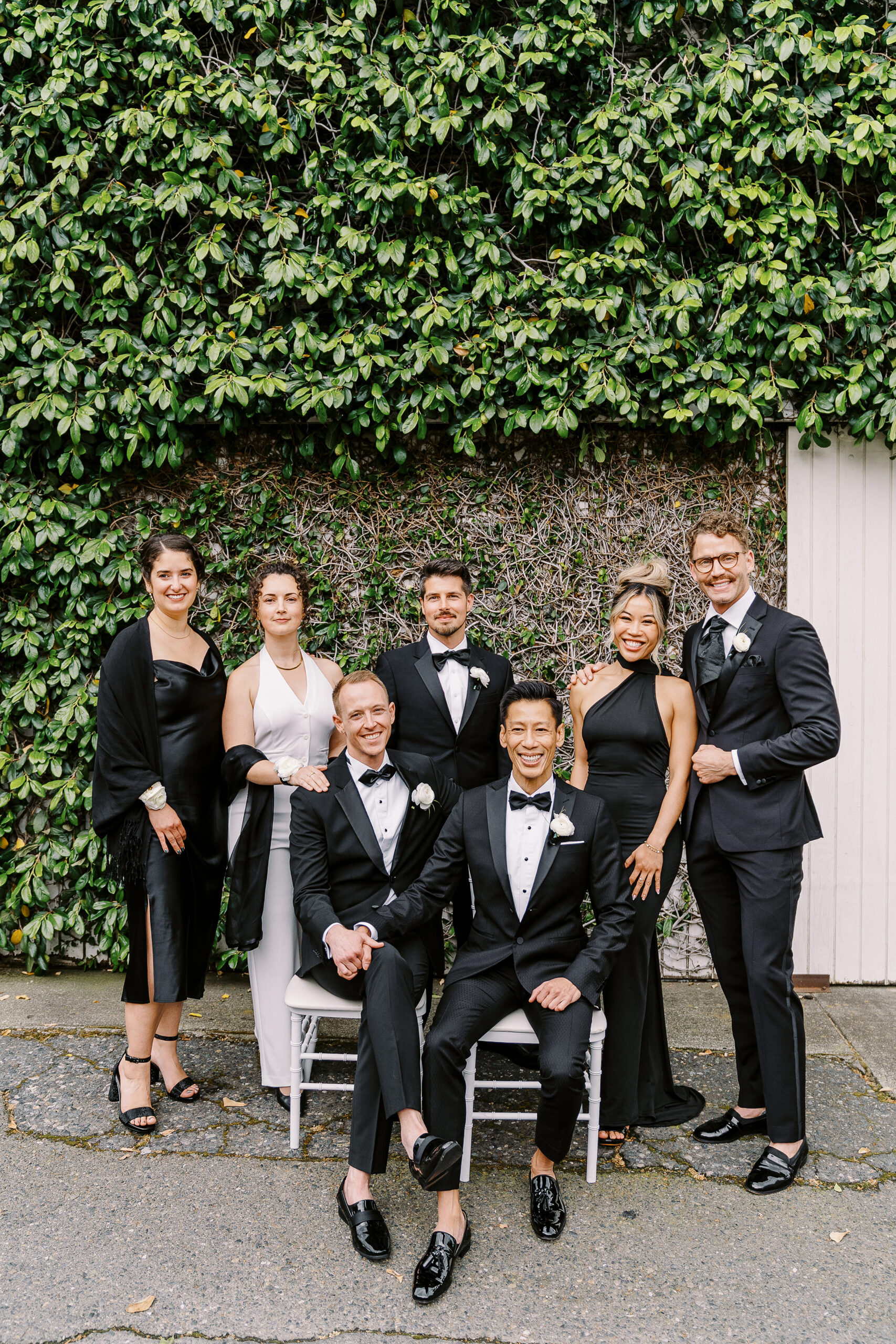 two grooms pose with their wedding party in sleek black tuxes at the vizcaya sacramento wedding venue