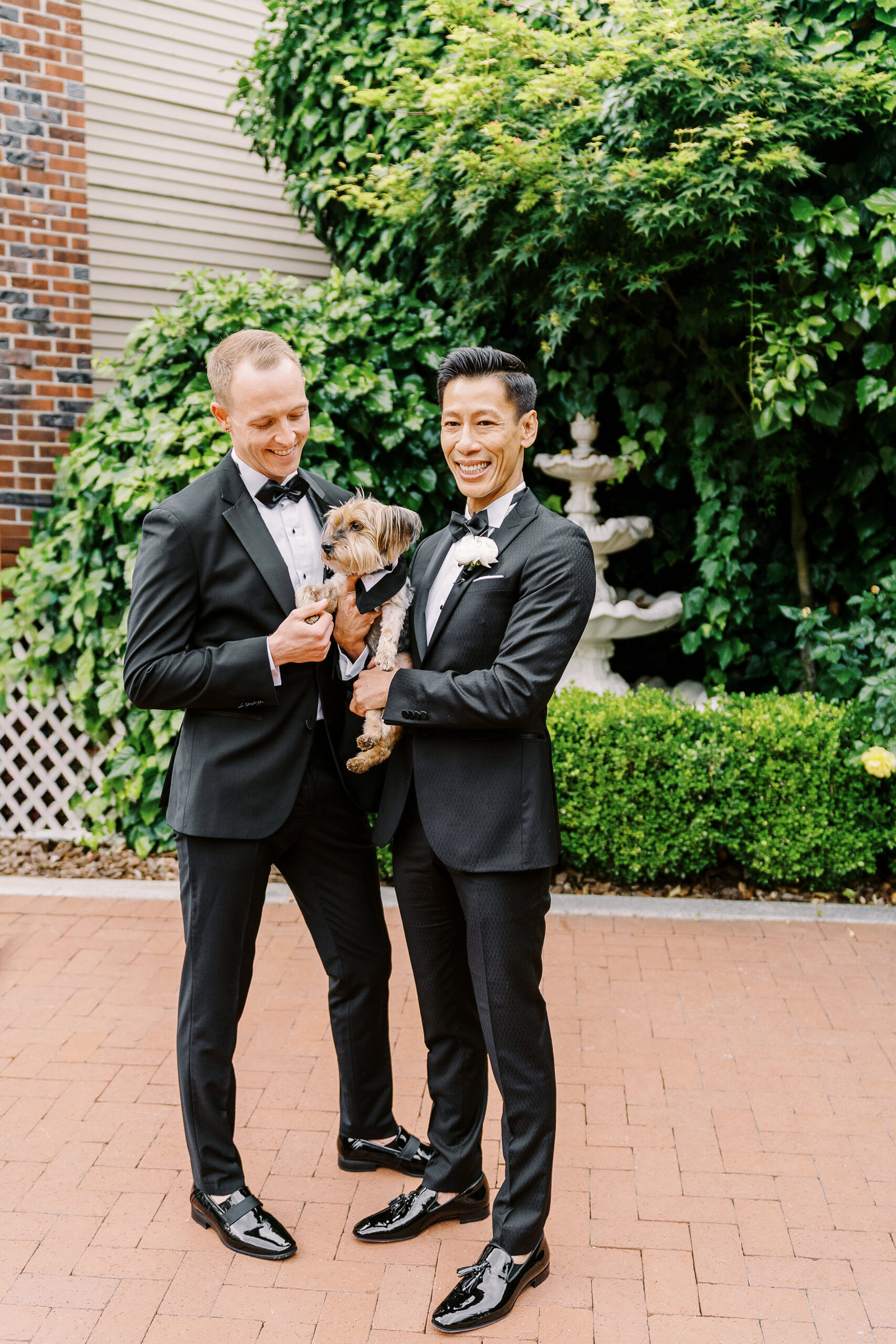 two grooms in black tuxes and bow ties pose for a portrait with their dog at the vizcaya sacramento wedding venue