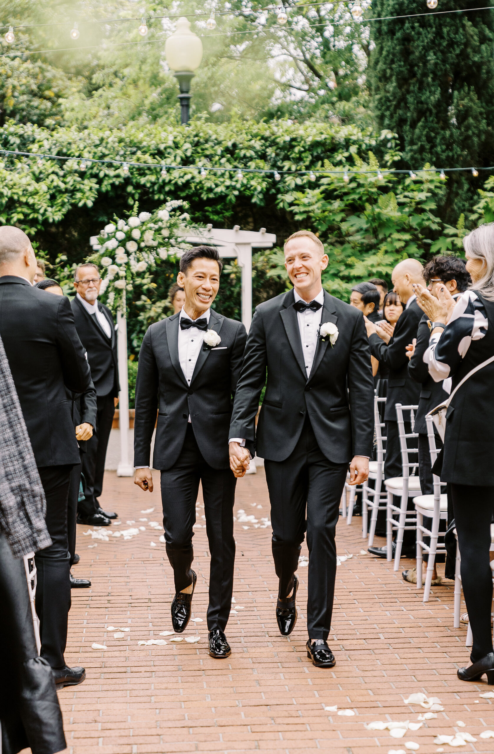 two grooms walk down the aisle holding hands at their vizcaya sacramento wedding ceremony