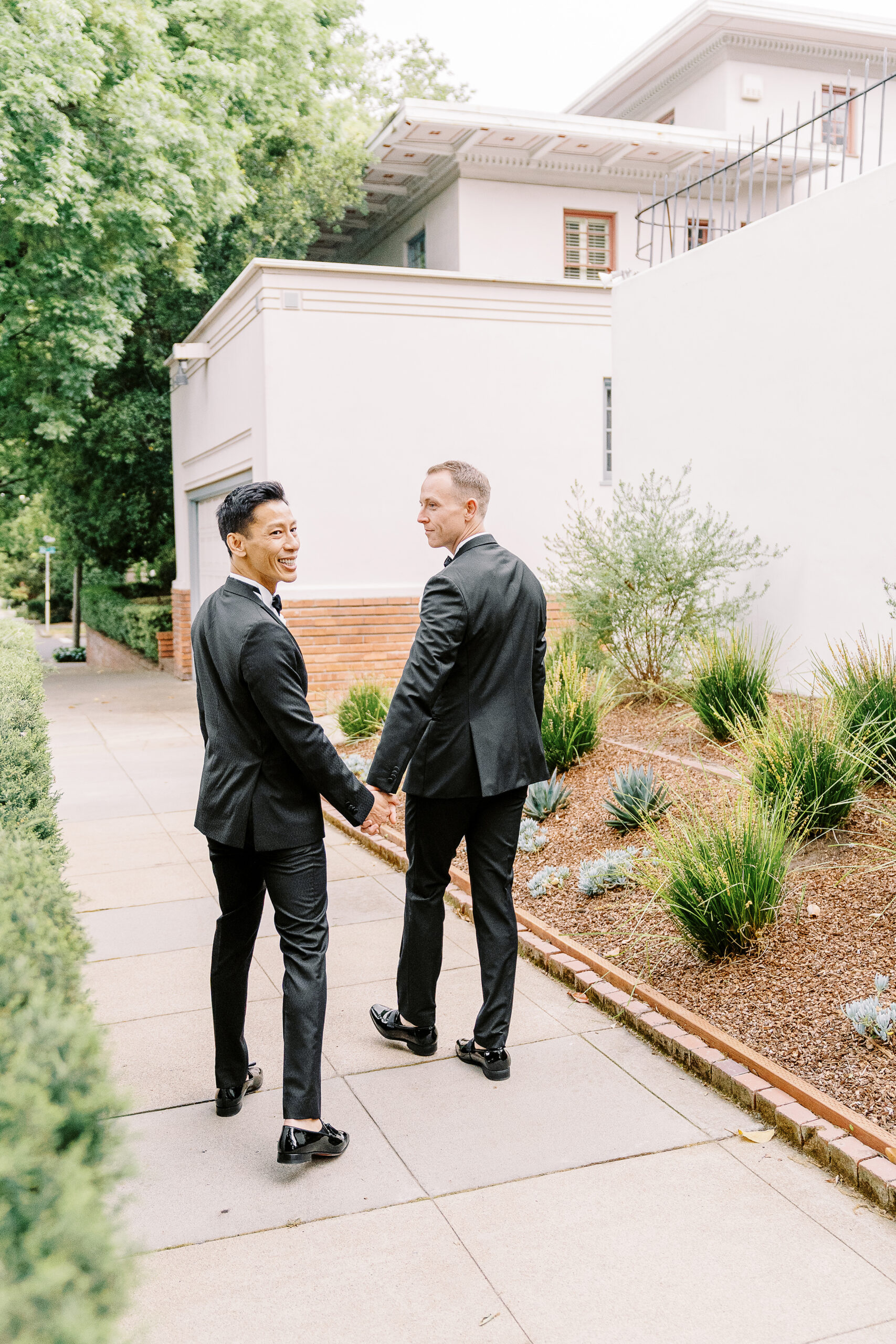 a groom looks over his shoulder while walking and holding hands with his new husband