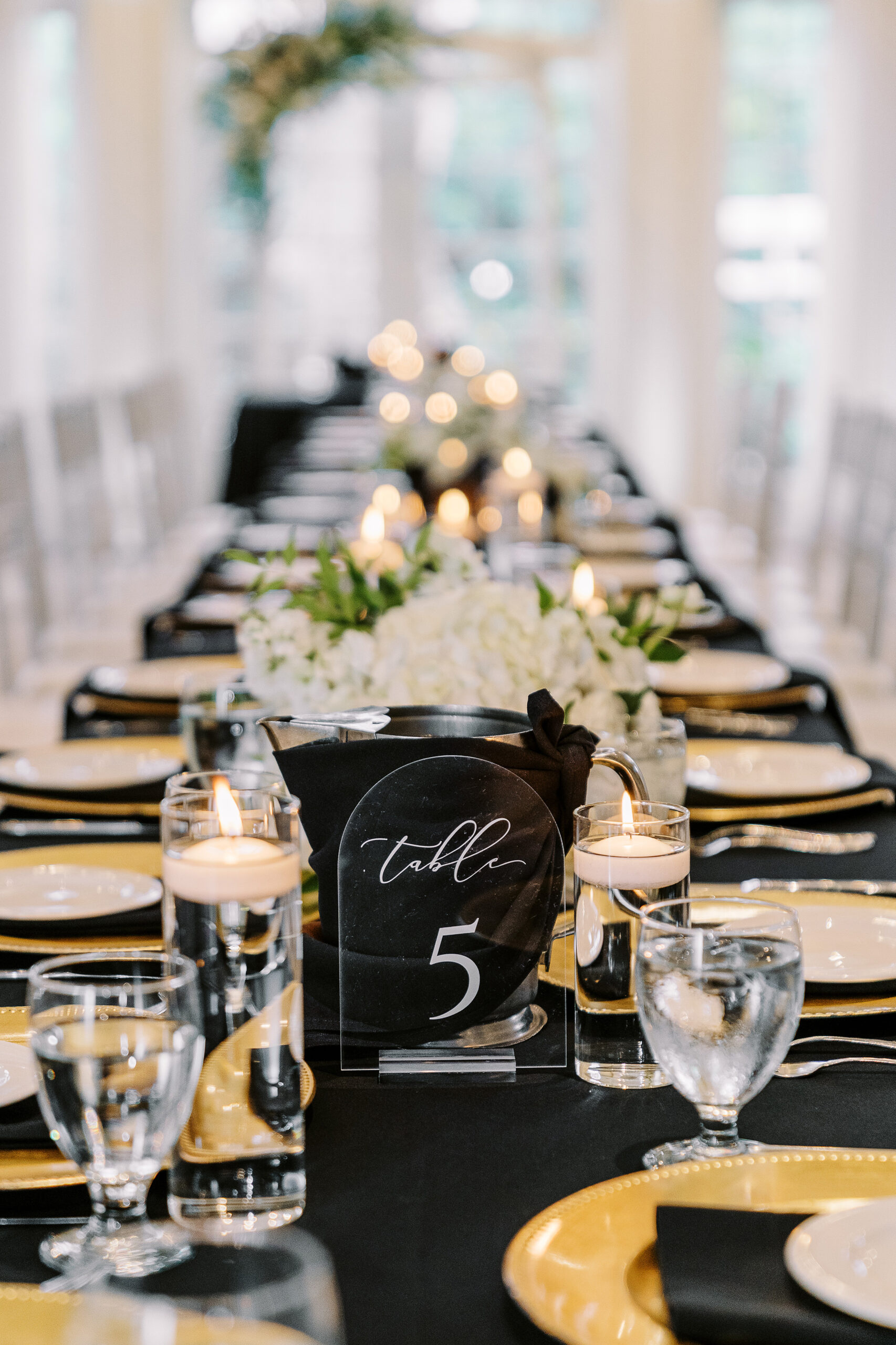 a reception set up at the vizcaya sacramento wedding venue featuring long tables with black linens, white flower arrangements, and gold plate chargers