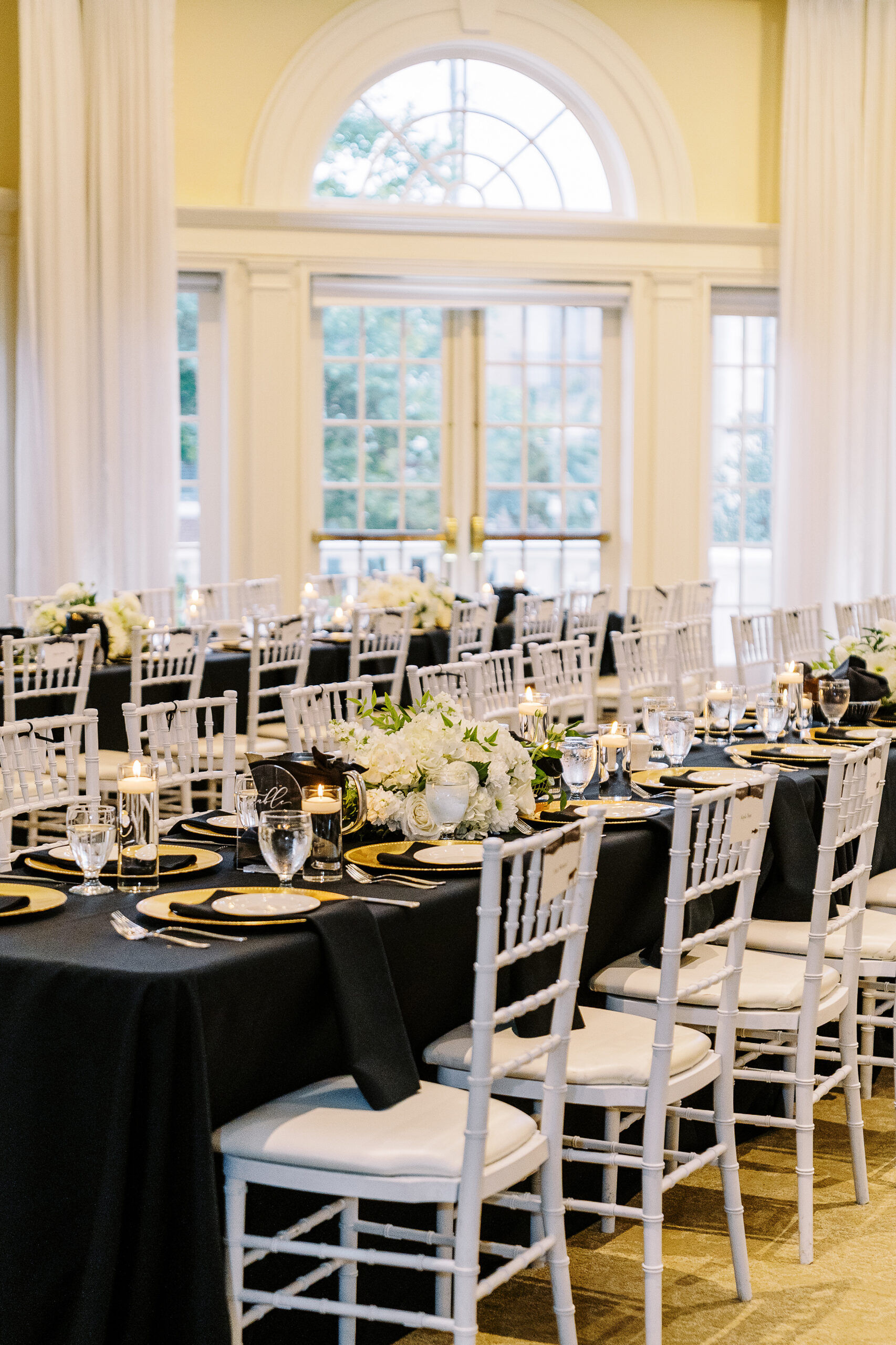 a reception set up at the vizcaya sacramento wedding venue featuring long tables with black linens, white flower arrangements, and gold plate chargers