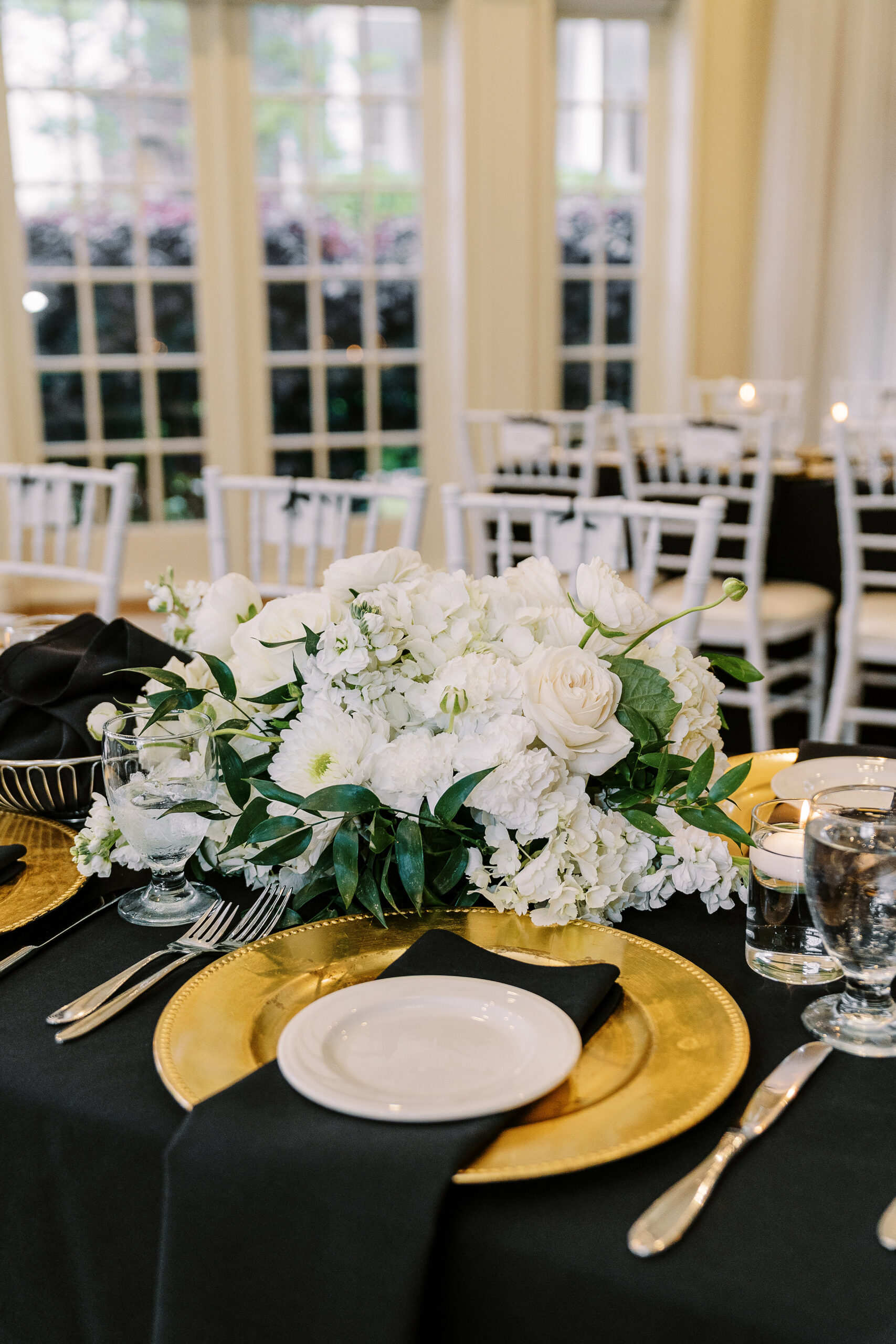 a reception set up at the vizcaya sacramento wedding venue featuring long tables with black linens, white flower arrangements, and gold plate chargers