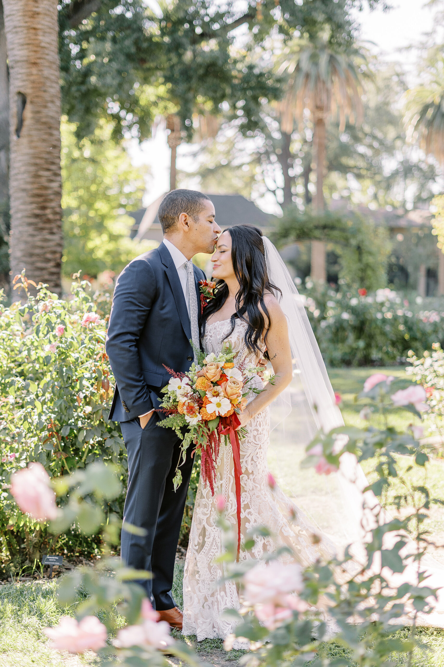 a groom kisses his bride on the forehead in the McKinley Park Rose Garden at their midtown Sacramento wedding photographed by Sacramento wedding photographer