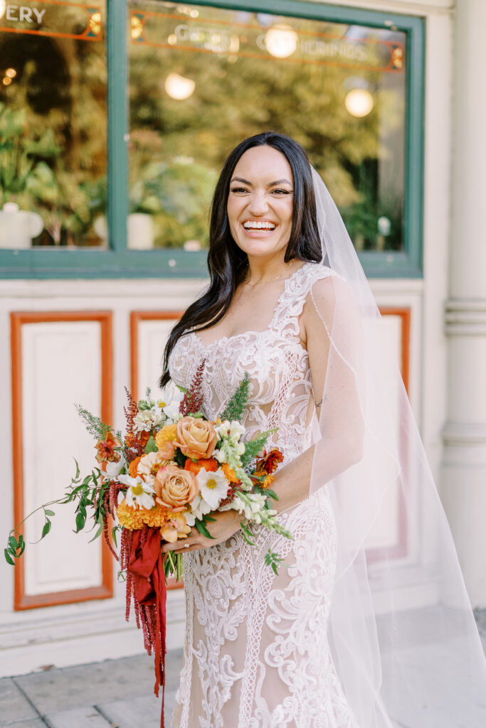 a bride holds her bouquet of orange and white flowers and laughs at her midtown Sacramento wedding photographed by Sacramento wedding photographer