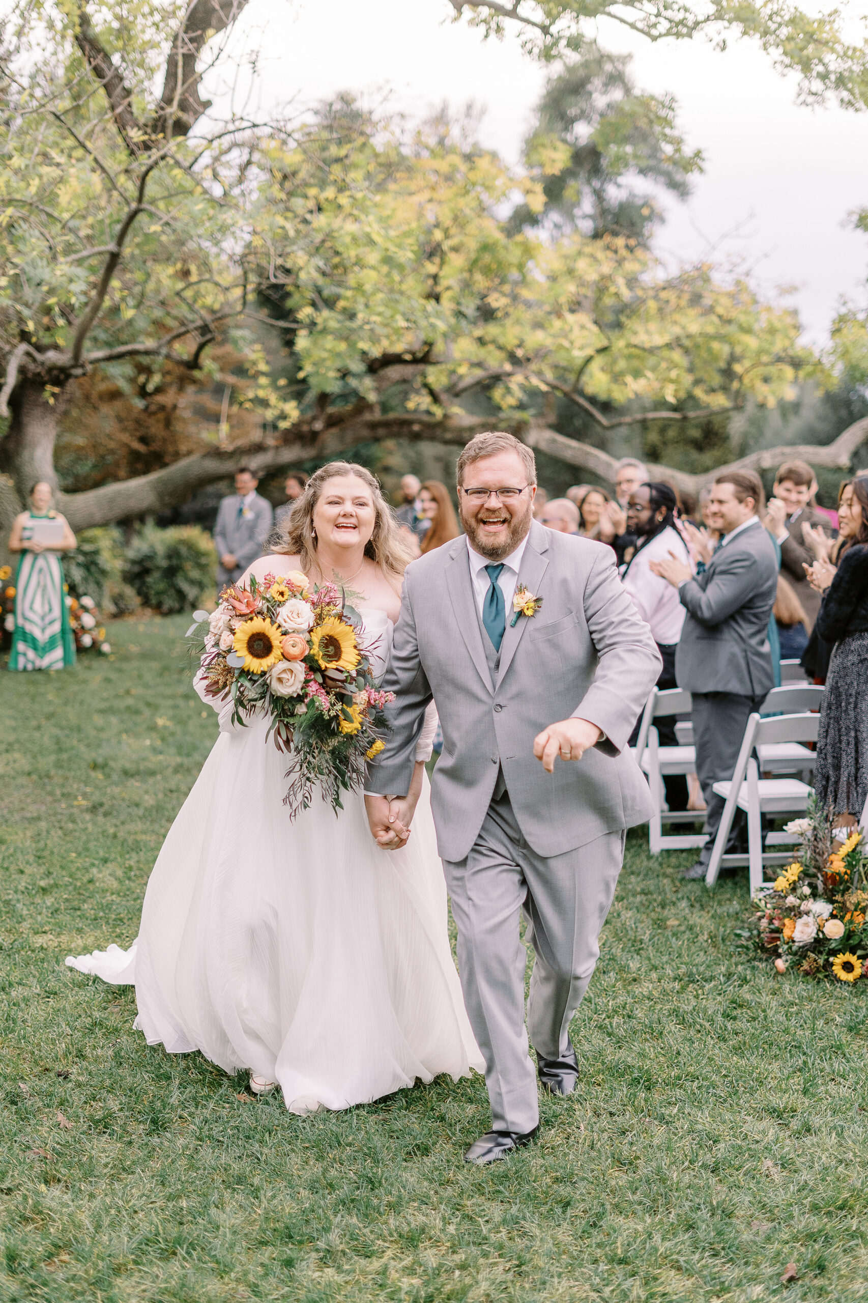 a bride and groom laugh and hold hands as they walk down their wedding ceremony aisle at The Maples Woodland photographed by Sacramento wedding photographer
